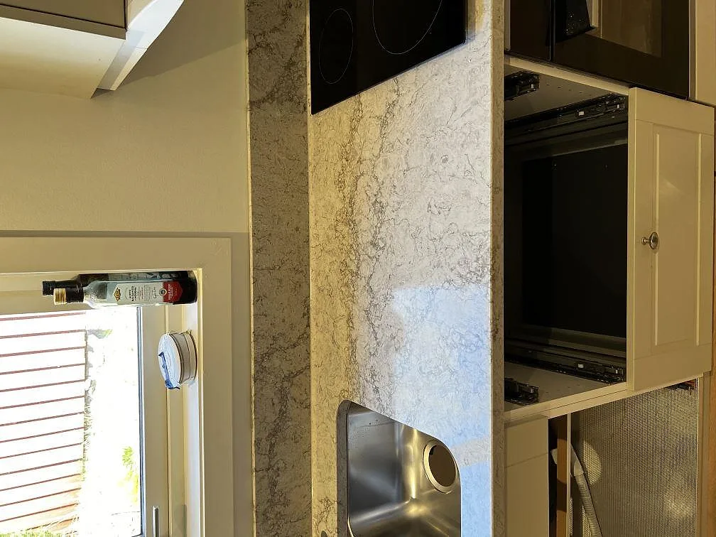 Köksbänkskiva i ljusgrå Caesarstone Moorland Fog, polerad, med underlimmad rostfri diskho och infälld induktionshäll i ett kök under montering i Trensum.