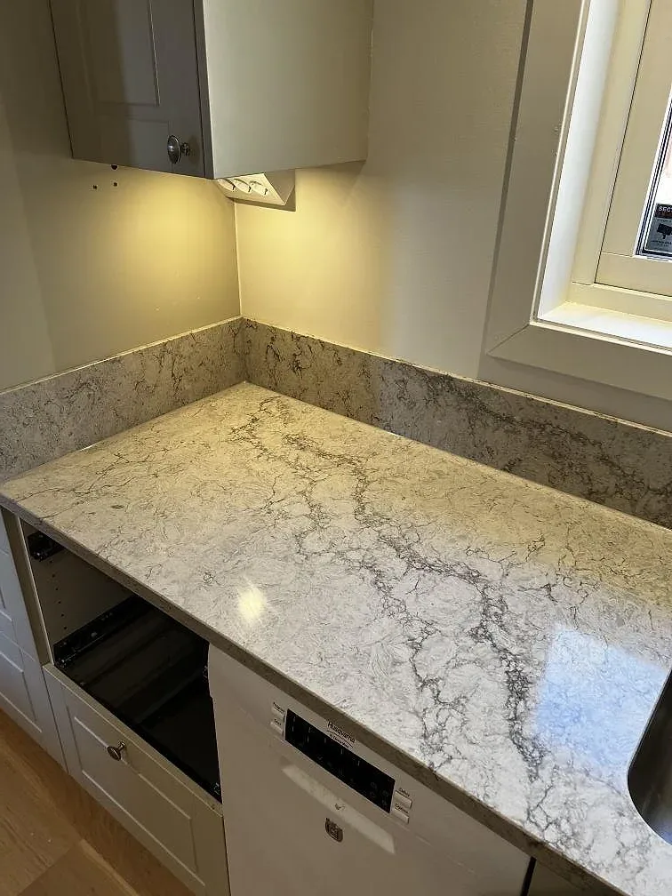 Översikt av kök i Trensum med köksbänkskiva i Caesarstone Moorland Fog, underlimmad rostfri diskho och induktionshäll under pågående montering.