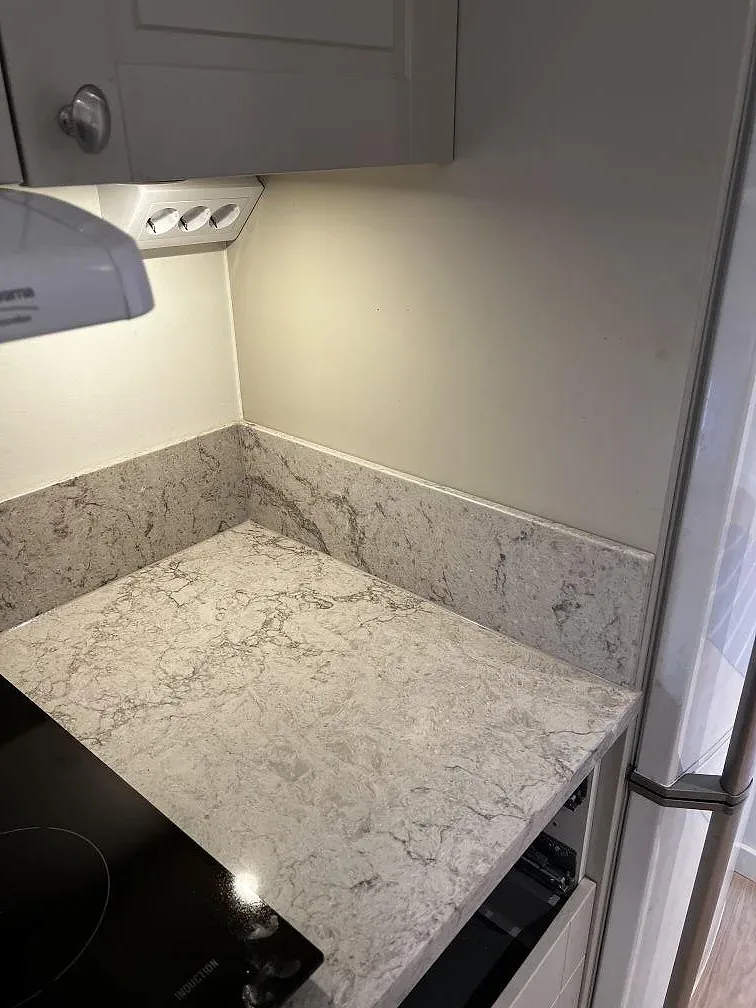 Infälld induktionshäll i polerad köksbänkskiva av Caesarstone Moorland Fog i ett kök i Trensum.