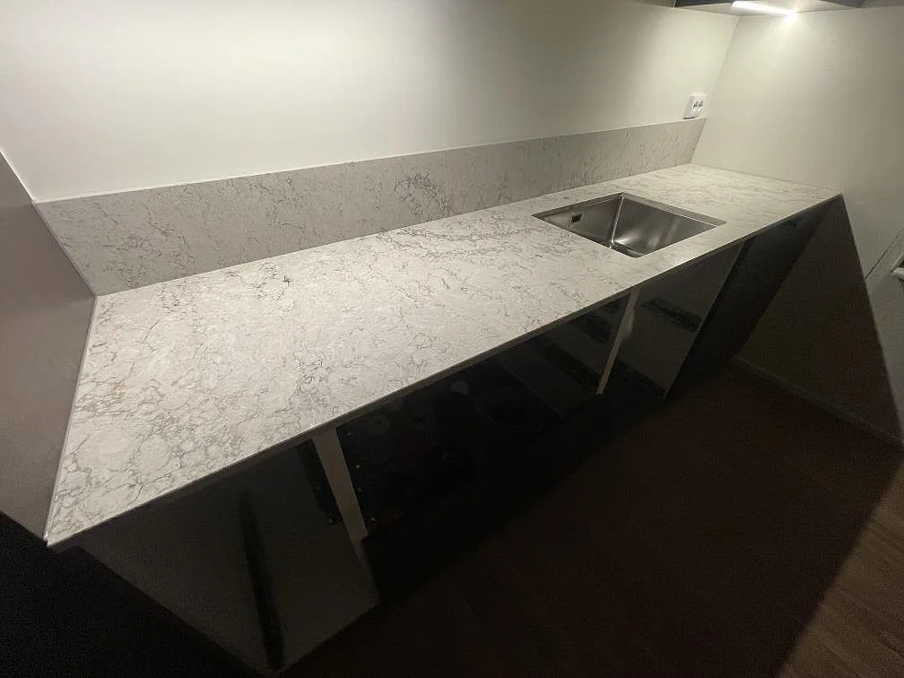 Köksbänkskiva i Caesarstone Moorland Fog längs fönsterväggen med underlimmad rostfri diskho och uppvikt stänkkant i ett kök i Tyresö.