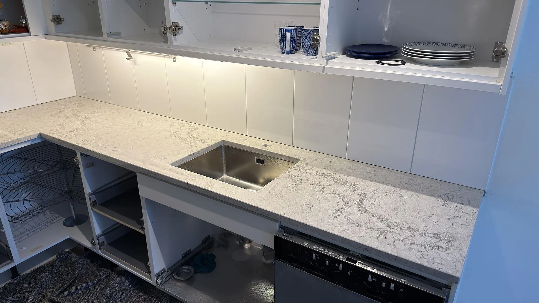 Närbild på polerad köksbänkskiva i Caesarstone Moorland Fog med underlimmad rostfri diskho och tydlig grå ådring i ett kök i Tyresöstrand.