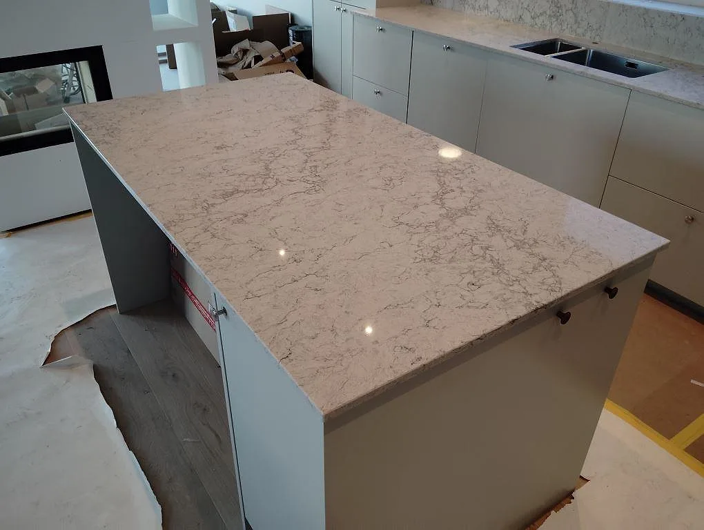 Stor köksö i Caesarstone Moorland Fog, polerad ljus kvartskomposit med grå ådring, framför väggbänk med rostfri diskho i ett kök i Vallentuna.