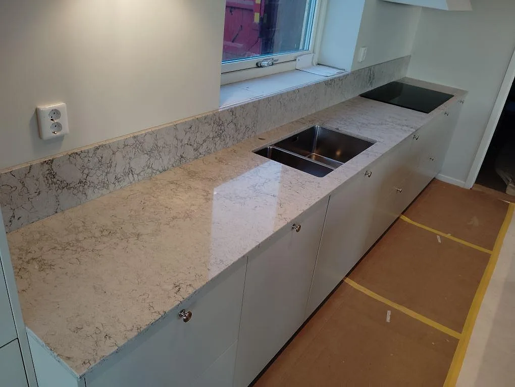 Väggbänk i Caesarstone Moorland Fog med rostfri diskho, svart häll och uppvikt stänkkant i ett ljust kök i Vallentuna.