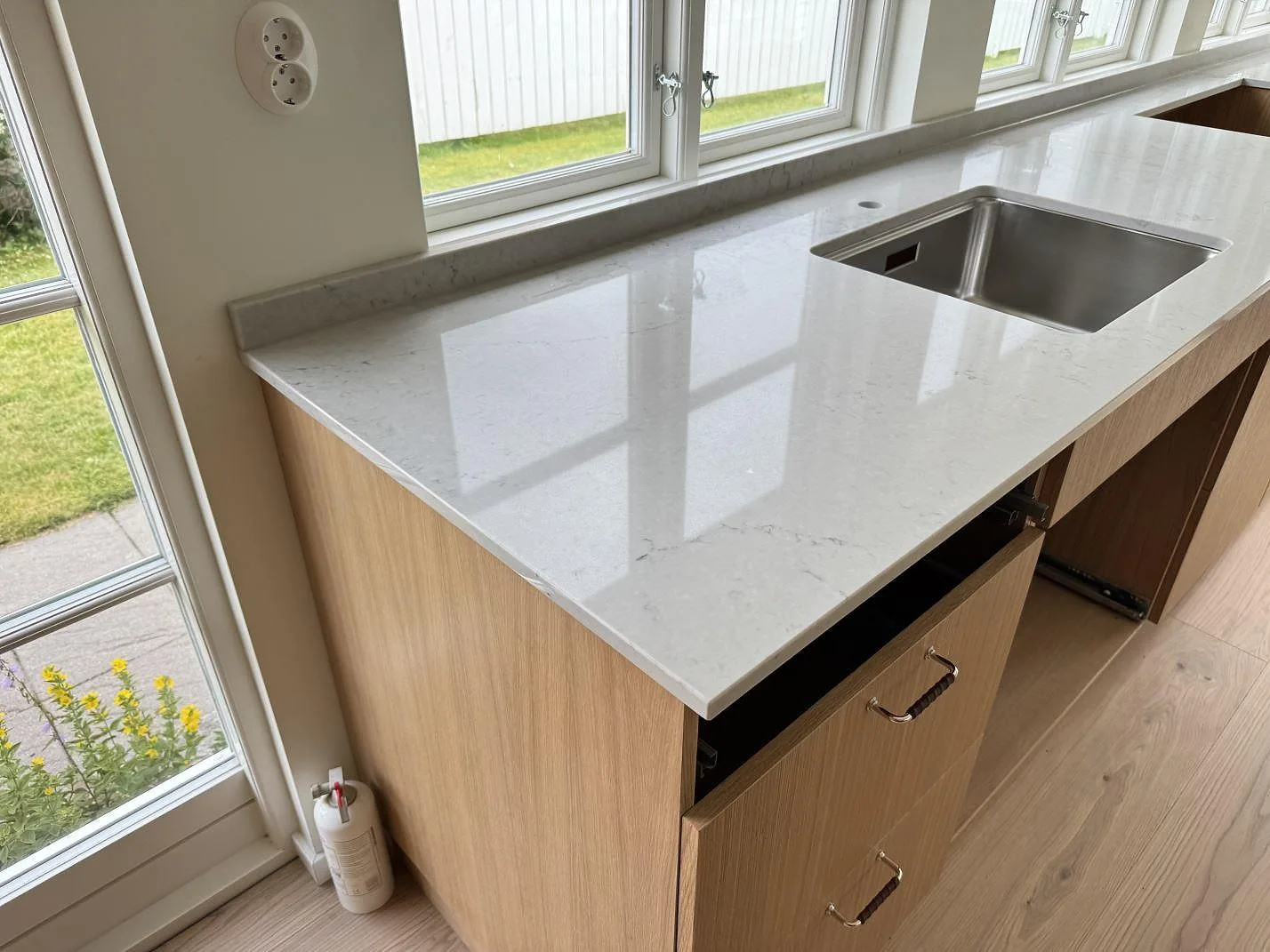 Köksbänkskiva i polerad Caesarstone Noble Grey med rostfri diskho och lågt stänkskydd vid fönster i Båstad.