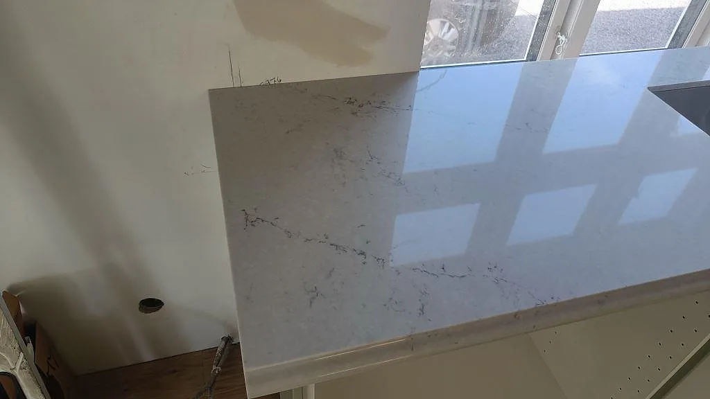 Detalj av ljus Caesarstone Noble Grey bänkskiva i komposit med polerad yta och grå ådring under montering i Ekeby.