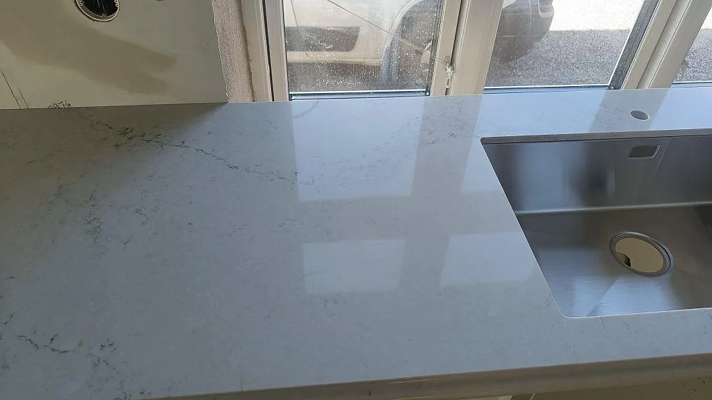 Närbild av polerad Caesarstone Noble Grey köksbänkskiva med rostfri diskho, hål för blandare och ljus ådring i Ekeby.