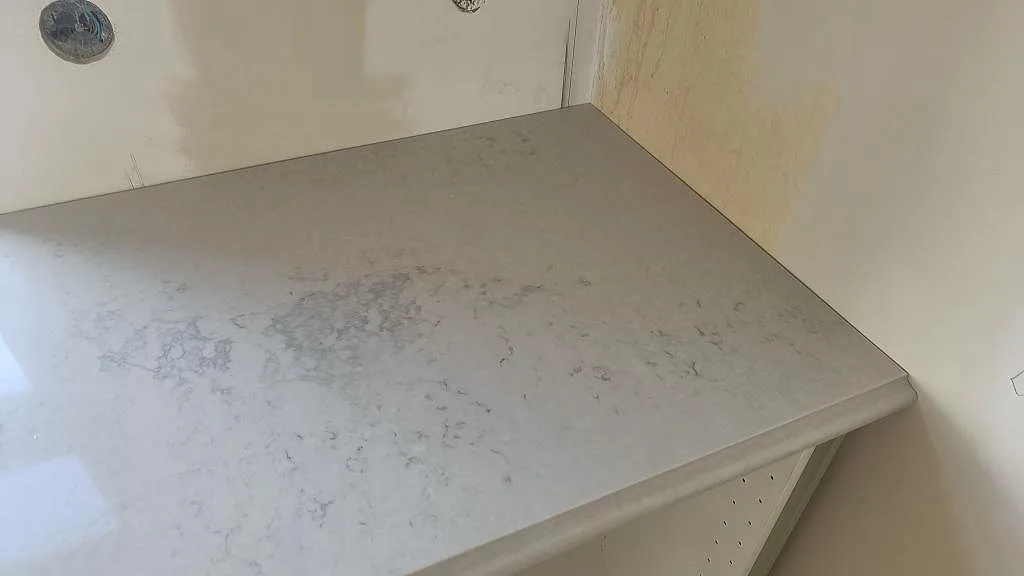 Hörnparti av polerad Caesarstone Noble Grey köksbänkskiva i komposit på vita stommar i Ekeby.