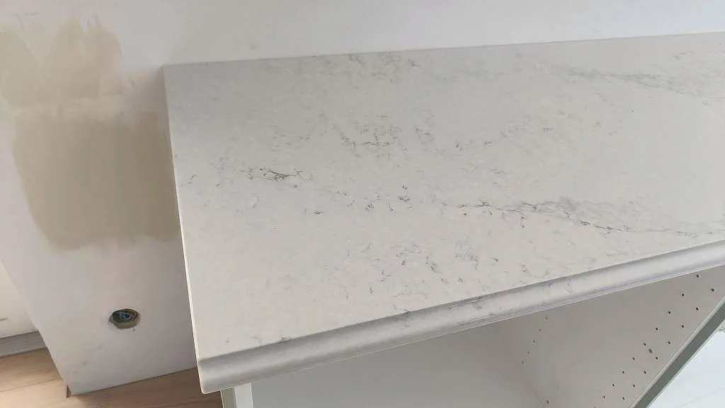 Närbild av framkant och ådring i polerad Caesarstone Noble Grey kompositbänkskiva i kök i Ekeby.