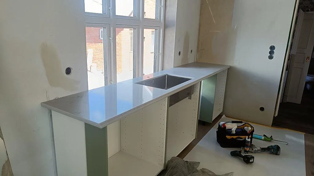 L-formad köksbänkskiva i Caesarstone Noble Grey komposit, polerad, med underlimmad rostfri diskho i ett kök i Ekeby.
