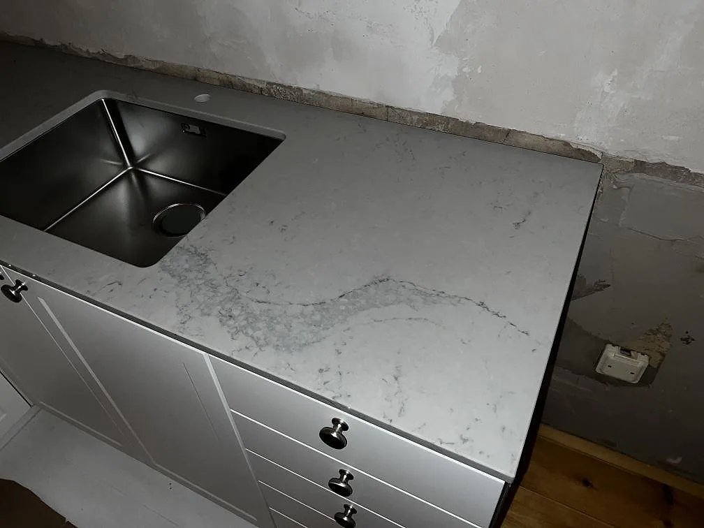 Närbild på polerad Caesarstone Noble Grey som köksbänkskiva med rostfri diskho och ljusa köksluckor i Helsingborg.