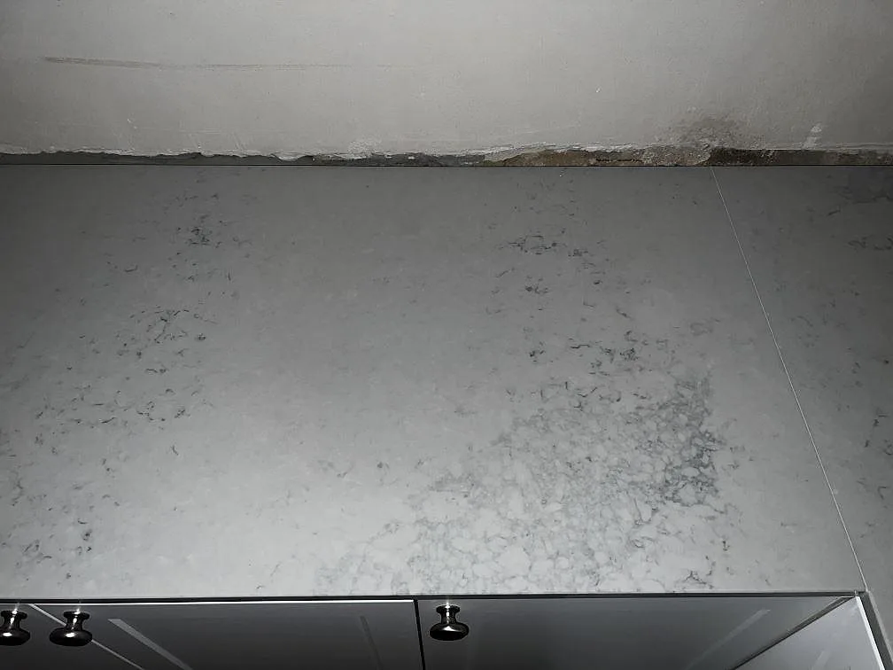Rak bänkskiva i polerad Caesarstone Noble Grey med diskret ådring och ljusa köksluckor i Helsingborg.