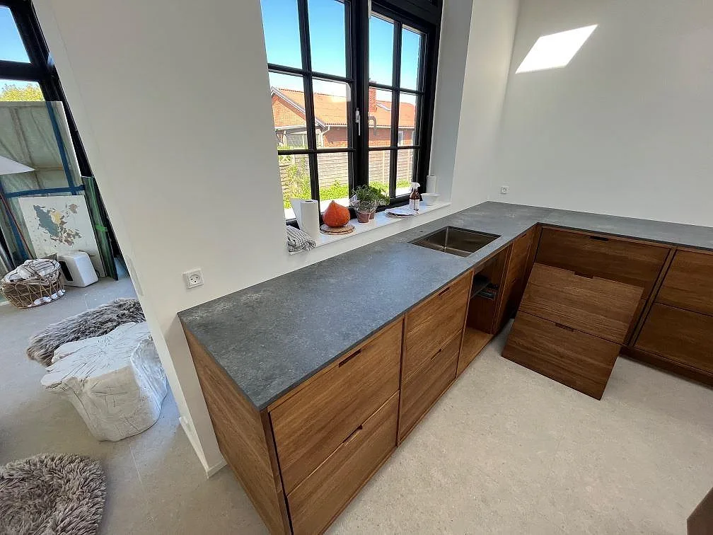 Köksbänkskiva i Caesarstone Rugged Concrete, matt grå kvartskomposit, på träskåp med stor fönsterfront i Kastrup.