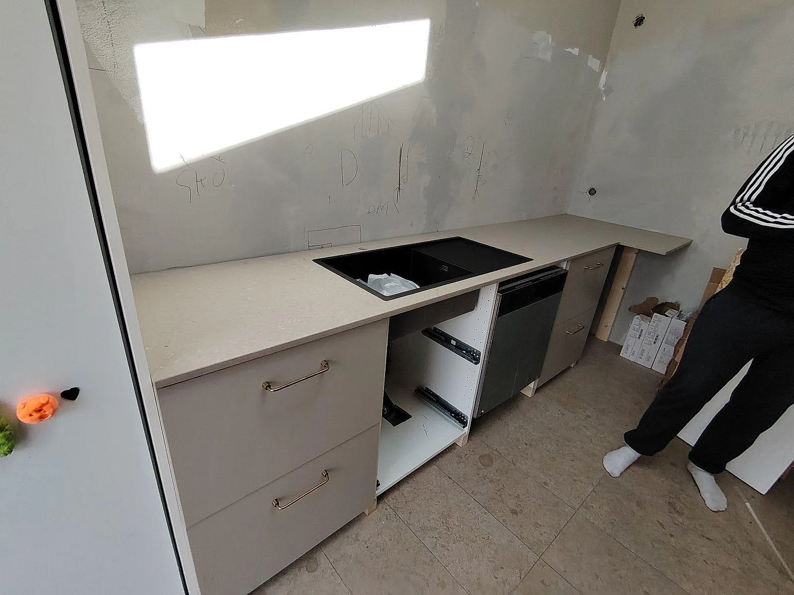 Rak köksbänkskiva i matt Caesarstone Shitake komposit längs ljusa skåpstommar i ett kök under montering i Enskede.