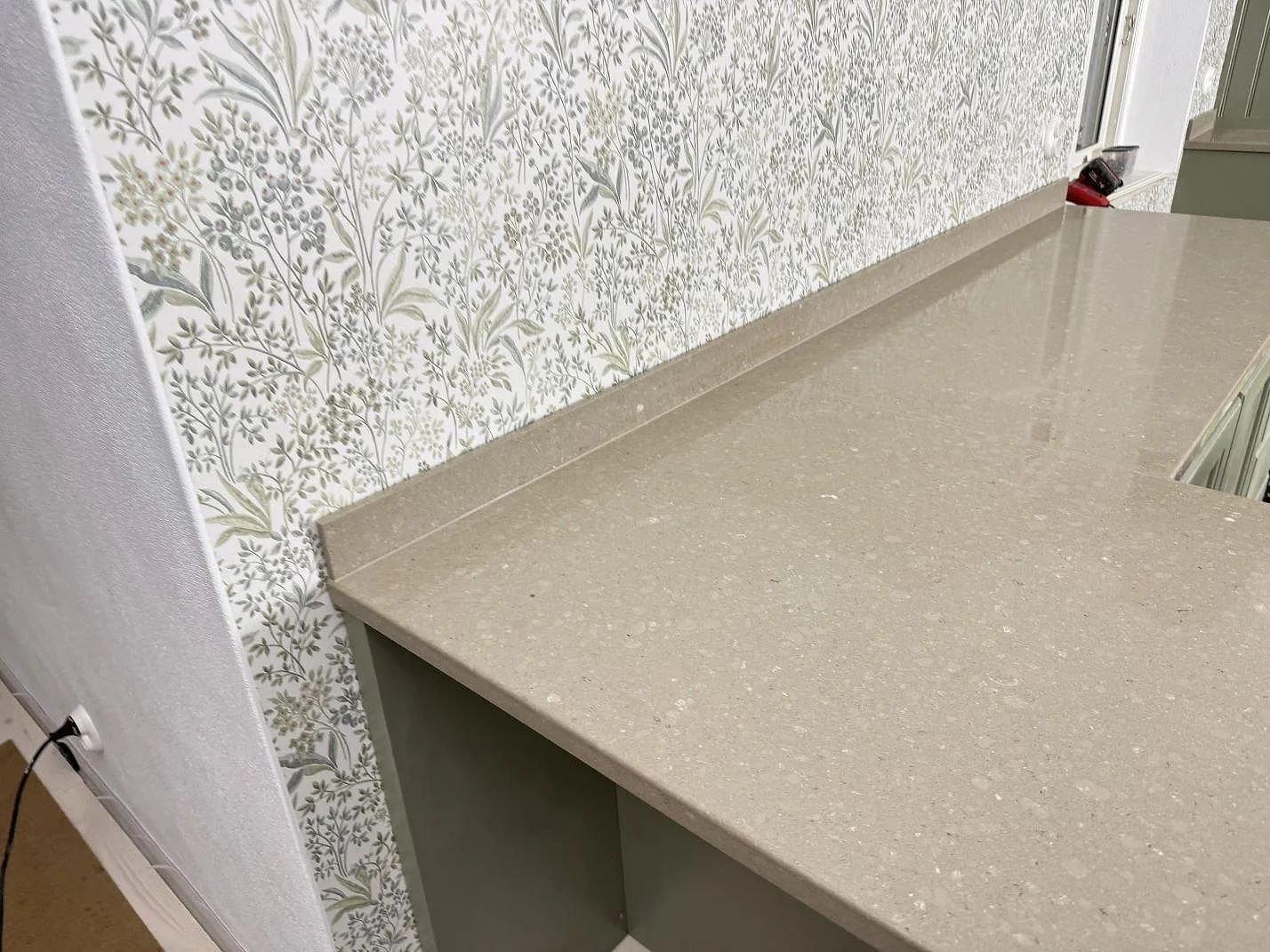 Detalj av polerad Caesarstone Shitake komposit med blank yta och uppvikt stänkkant mot mönstrad vägg i Hörby.