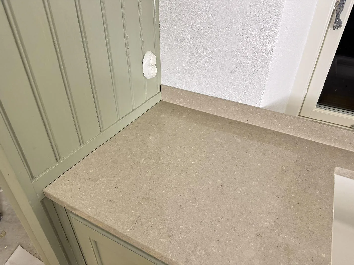 Hörnparti av Caesarstone Shitake bänkskiva med polerad yta, låg stänkkant och grön köksinredning i Hörby.
