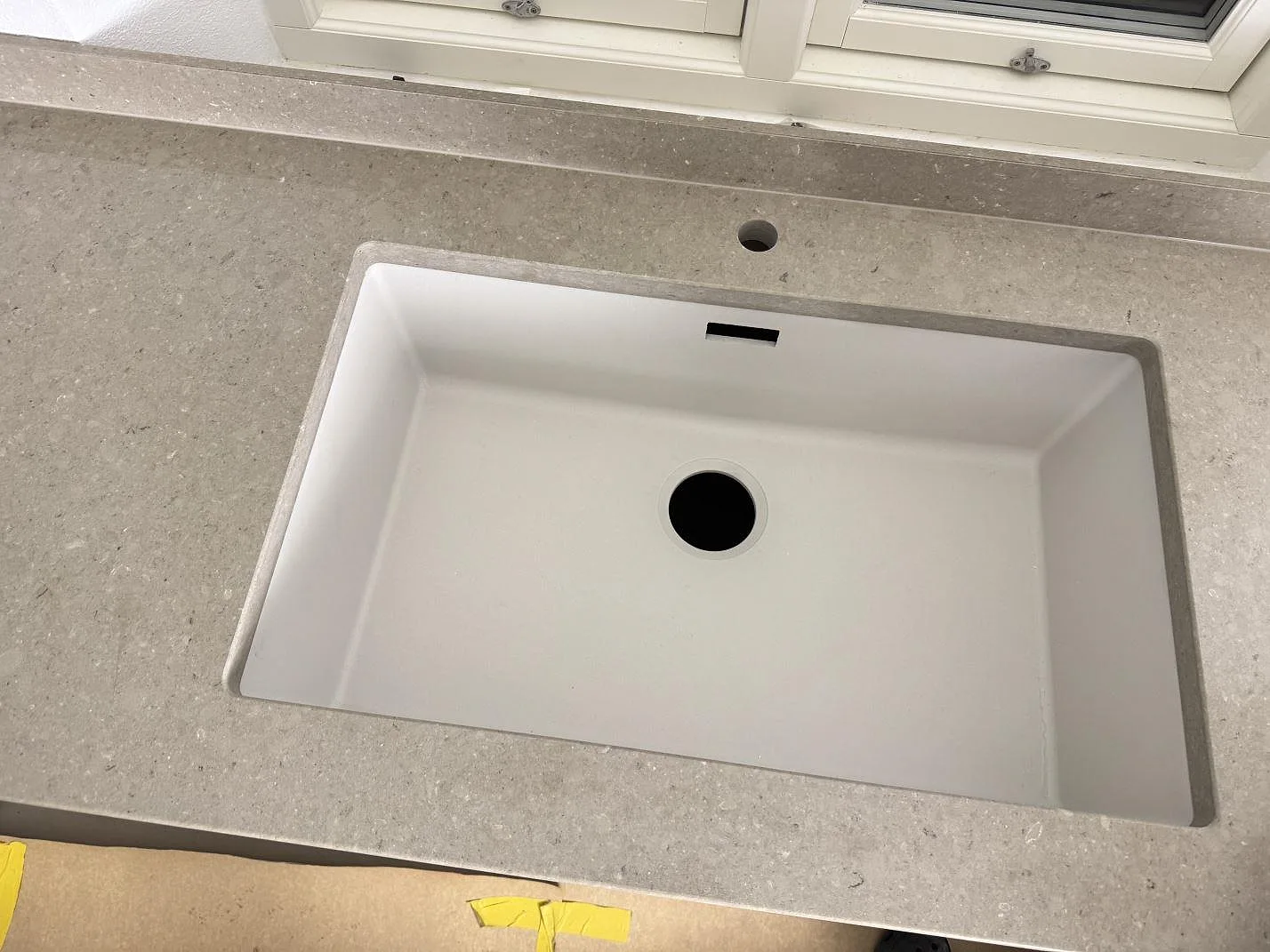 Närbild på vit diskho i en polerad Caesarstone Shitake bänkskiva med blandarhål vid fönster i ett kök i Hörby.