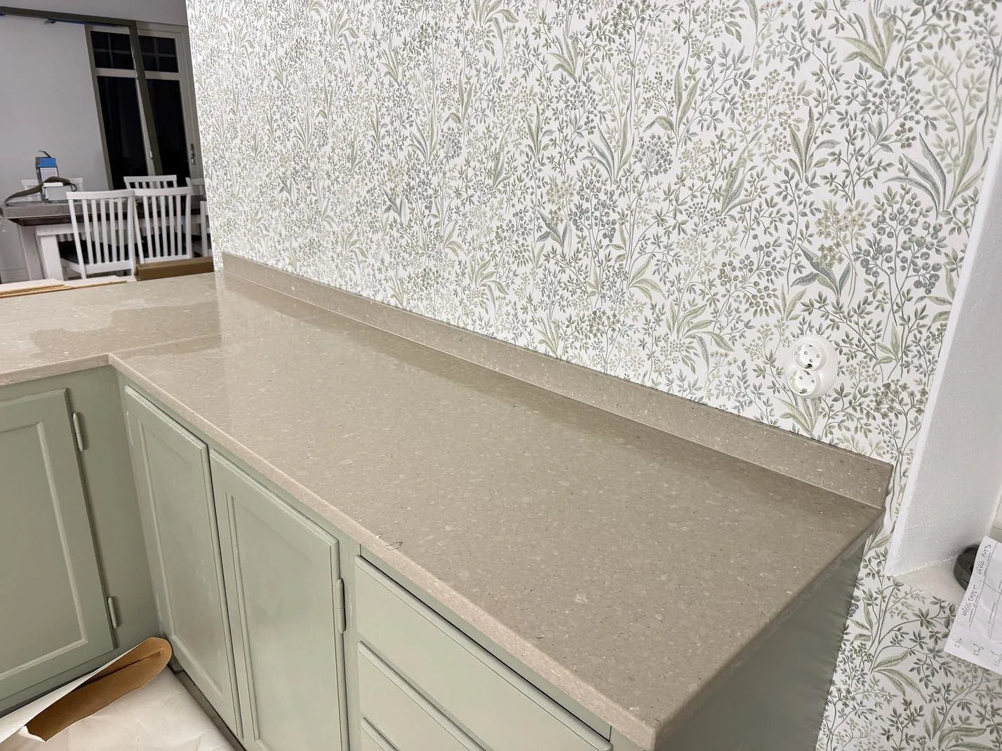 Polerad köksbänkskiva i Caesarstone Shitake längs mönstrad vägg, med gråbeige komposityta och låg stänkkant i Hörby.