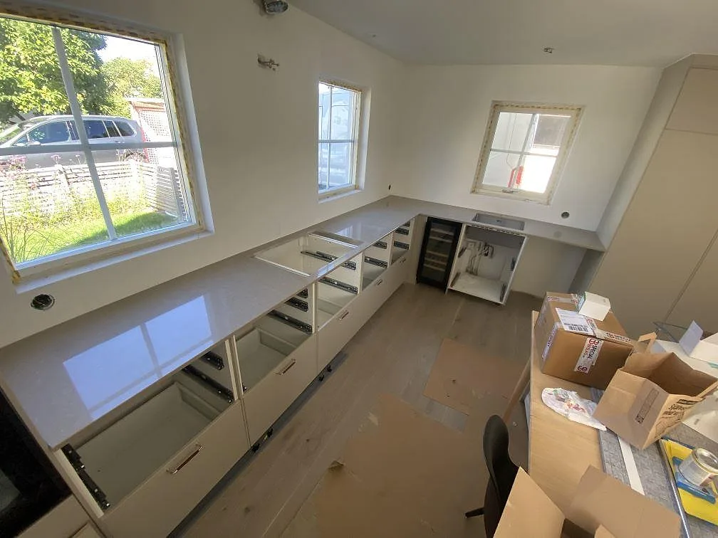 Köksbänkskiva i Caesarstone Shitake, polerad greige kvartskomposit, i ett L-format kök under montering i Limhamn.