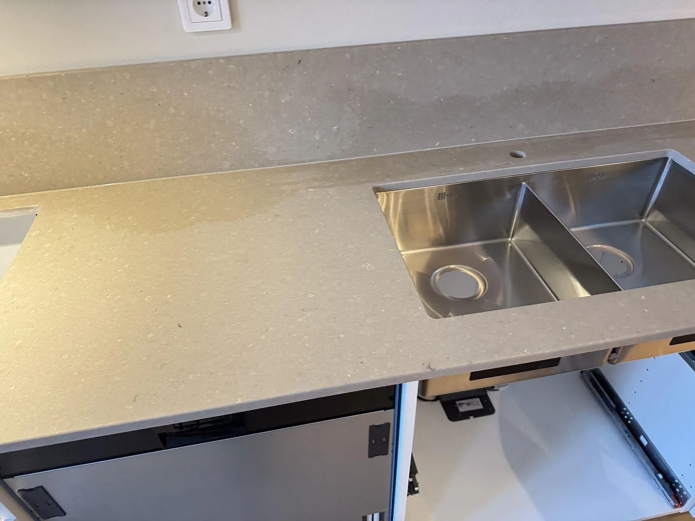 Köksbänkskiva i Caesarstone Shitake, varm gråbeige kvartskomposit med matt yta, med underlimmad dubbelho i rostfritt stål och uppvikt stänkskydd i ett kök i Malmö.