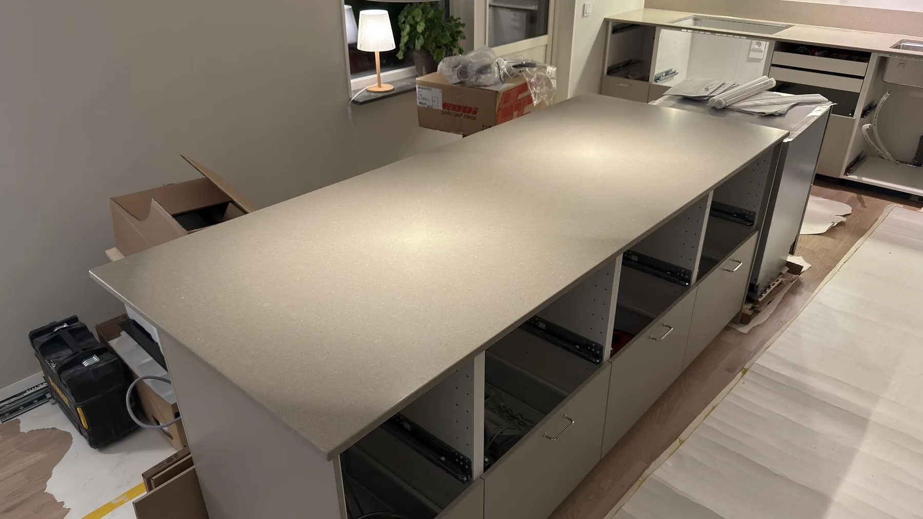 Köksö i matt Caesarstone Shitake sedd från sidan, med öppna stommar och bänkrad längs väggen i ett kök under montering i Örebro.