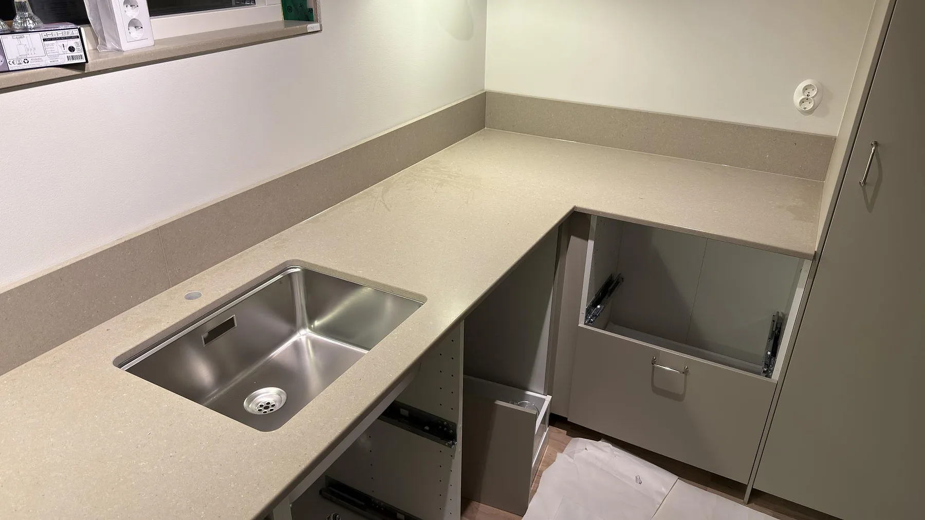 Underlimmad rostfri diskho i en L-formad köksbänk i matt Caesarstone Shitake med uppvikt stänkkant i ett kök i Örebro.