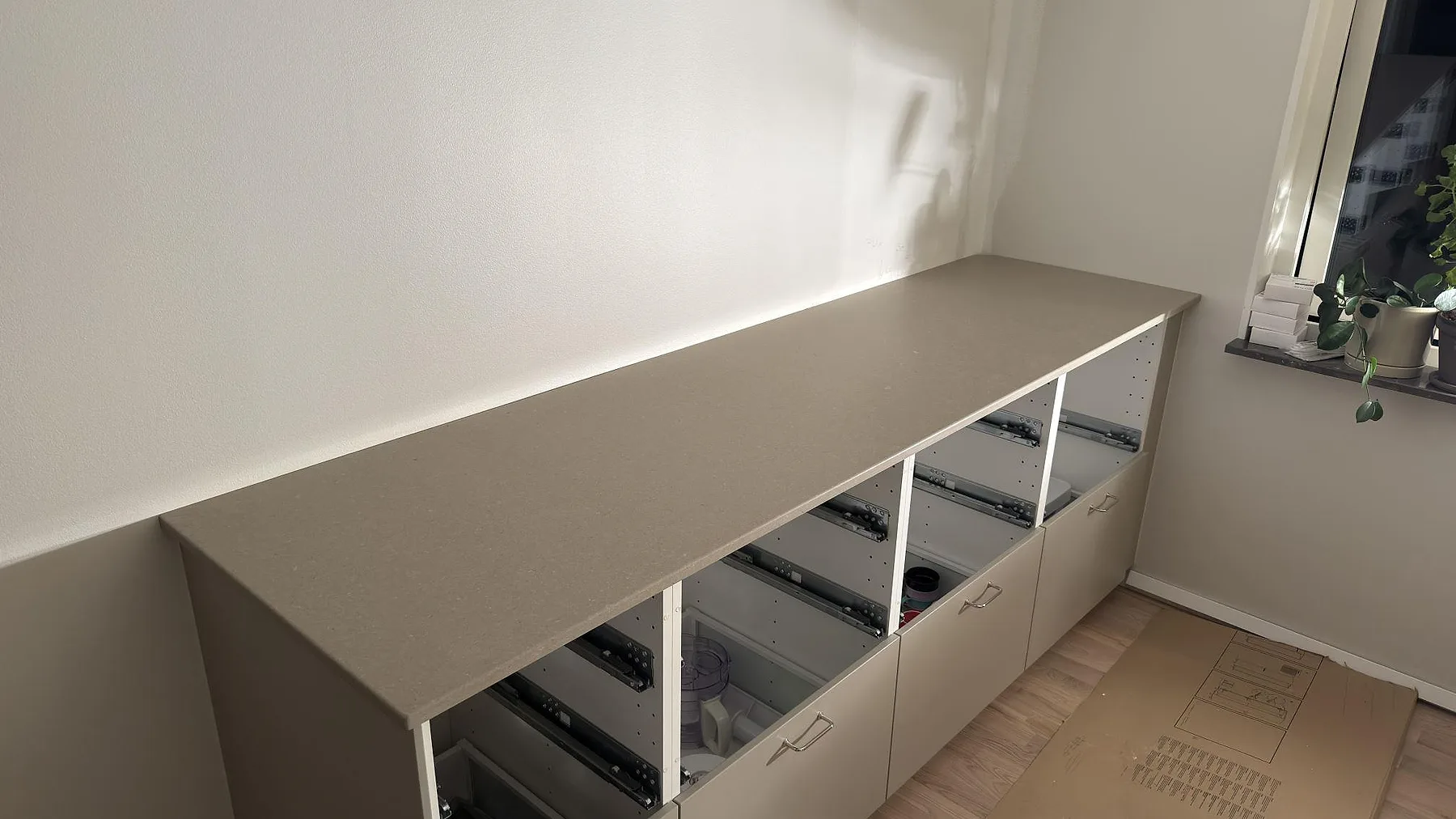Lång köksbänkskiva i Caesarstone Shitake, matt taupebrun kvartskomposit, monterad på stommar med uppvikt stänkkant i ett kök i Örebro.