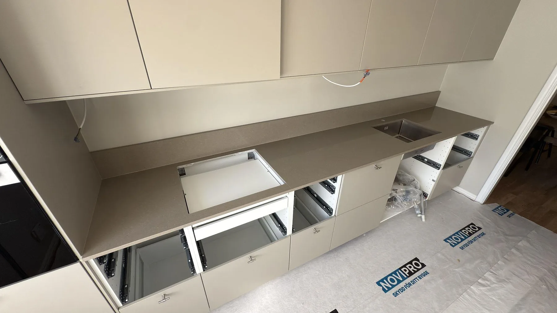 Köksbänkskiva i Caesarstone Shitake, en varm beige kvartskomposit med polerad yta, monterad i en lång rak linje med underlimmad rostfri diskho i ett kök under montering i Täby.