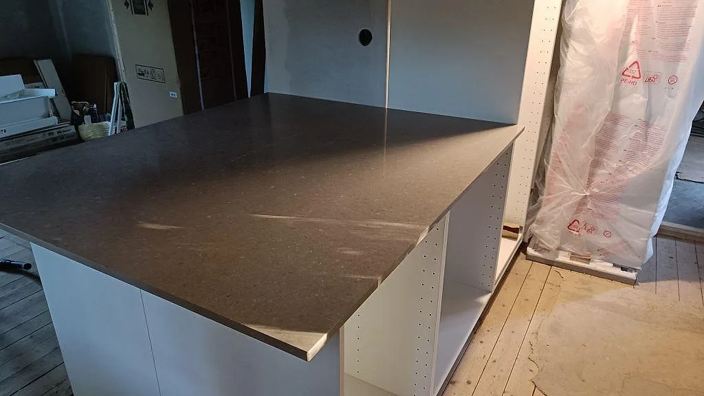 Köksö i polerad Caesarstone Shitake, taupegrå kvartskomposit, med synlig stenkant i ett kök under montering i Västra Frölunda.