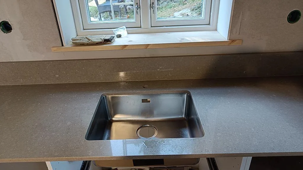Närbild på polerad Caesarstone Shitake runt en rostfri diskho och låg stänkkant under fönstret i Västra Frölunda.