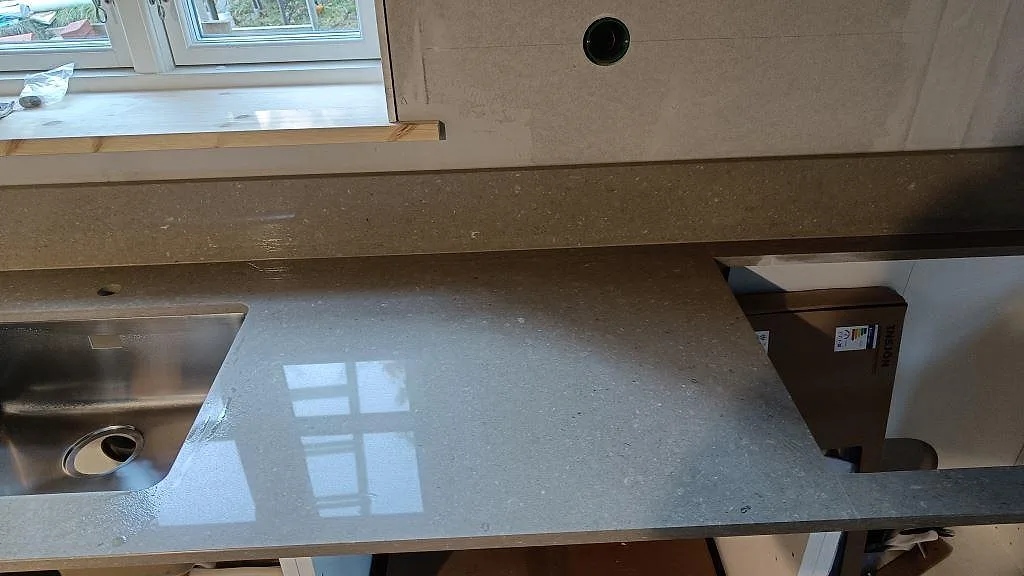 Polerad bänkskiva i Caesarstone Shitake med synlig diskho och förlängd arbetsyta längs fönsterväggen i Västra Frölunda.