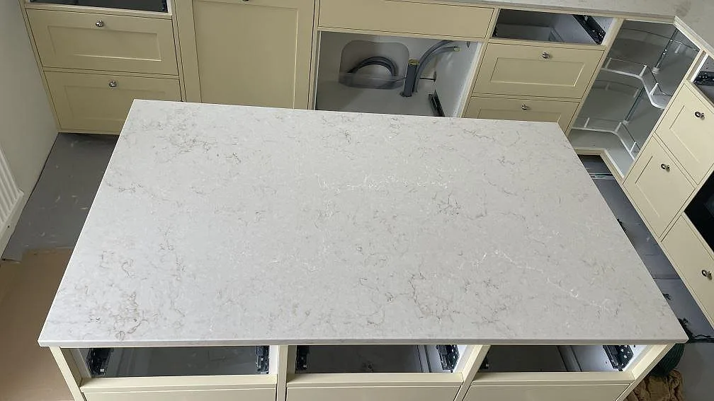 Närbild på köksö i polerad Caesarstone Taj Royale 5212, ljus komposit med mjuk ådring monterad på köksstommar i Höllviken.
