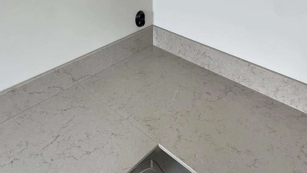 Hörnparti i kök med polerad Caesarstone Taj Royale 5212, ljus kompositbänkskiva och låg stänkkant i Höllviken.
