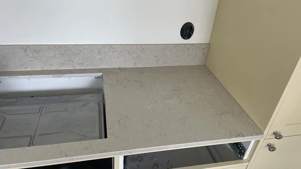 Sidoyta vid hällurtag i polerad Caesarstone Taj Royale 5212, ljus komposit med stänkkant och öppna köksstommar i Höllviken.