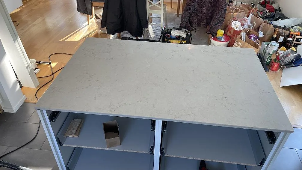 Närbild av köksö i Caesarstone Taj Royale 5212, polerad komposit med mjuk grå ådring under montering i Lomma.