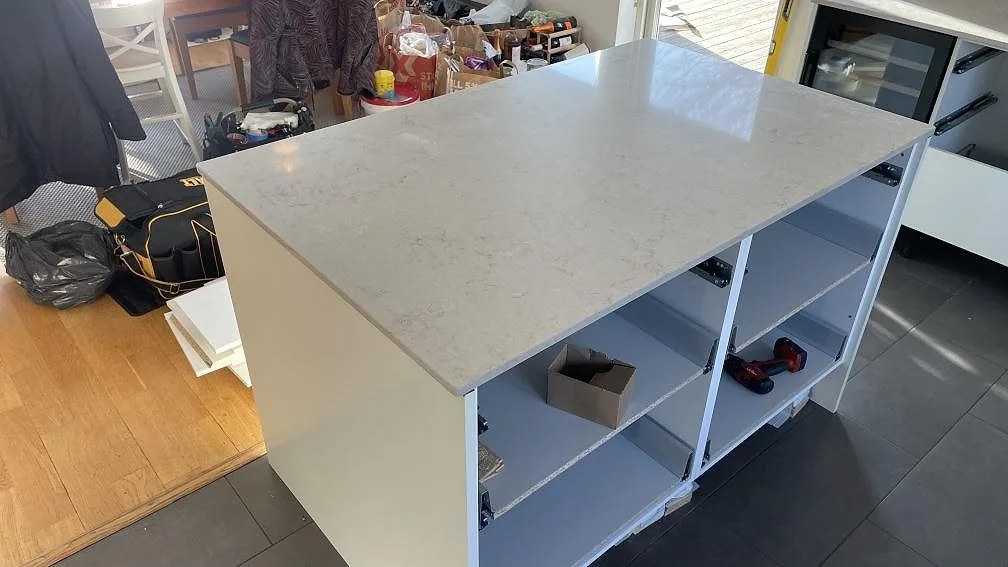Köksö med polerad Caesarstone Taj Royale 5212 i ljus kompositsten, monterad på öppna köksstommar i Lomma.