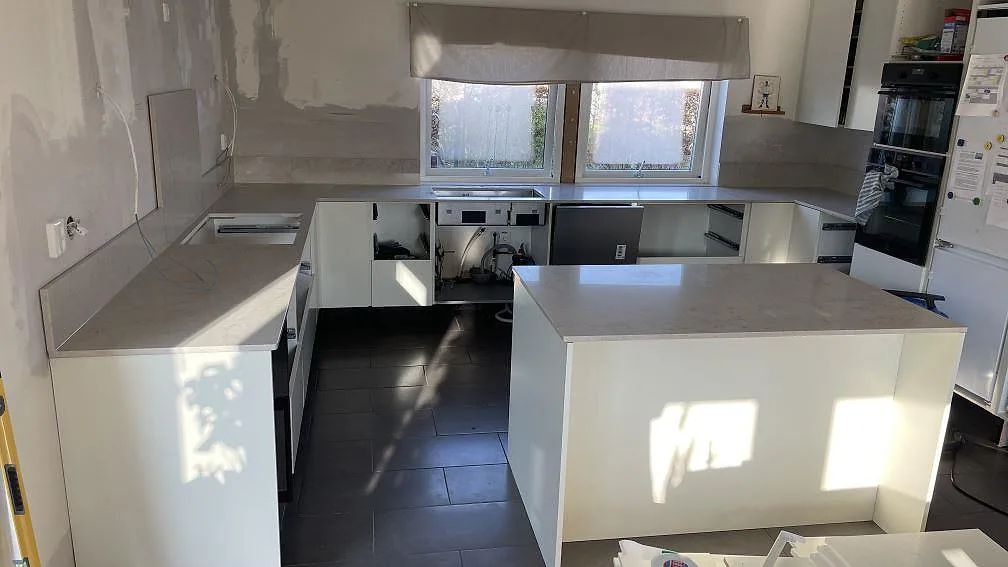 Köksbänkskiva i polerad Caesarstone Taj Royale 5212 med köksö, väggbänkar och stänkskydd i ett kök i Lomma.