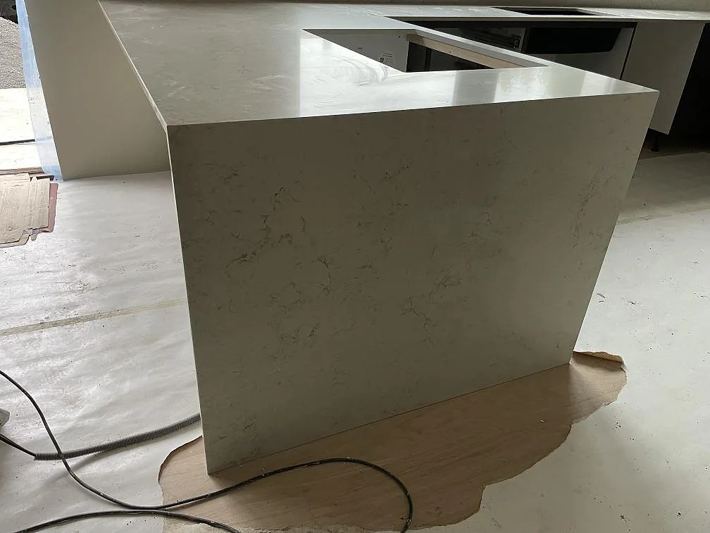 Detalj av vattenfallsida och blank bänkyta i Caesarstone Taj Royale 5212, polerad komposit, i ett kök under montering i Nacka.
