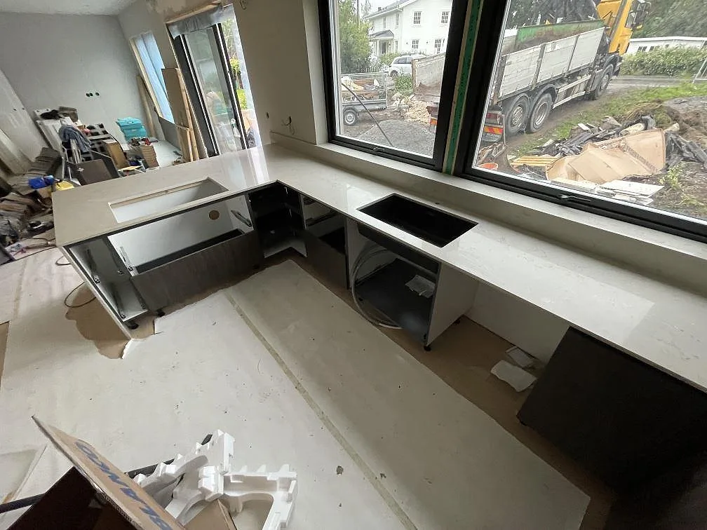 Lång väggbänk och utskjutande köksdel i Caesarstone Taj Royale 5212, 20 mm polerad komposit, monterad vid fönster i Nacka.