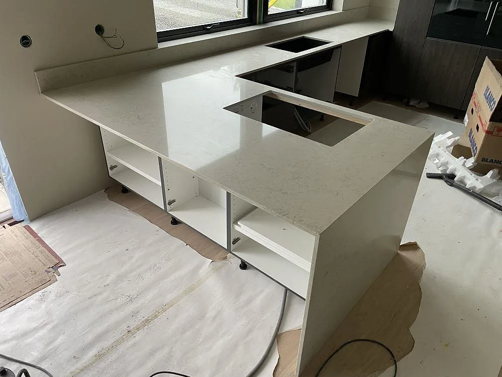 Köksbänkskiva i Caesarstone Taj Royale 5212, polerad komposit, med låg stänkkant och förberedda urtag i ett kök under montering i Nacka.
