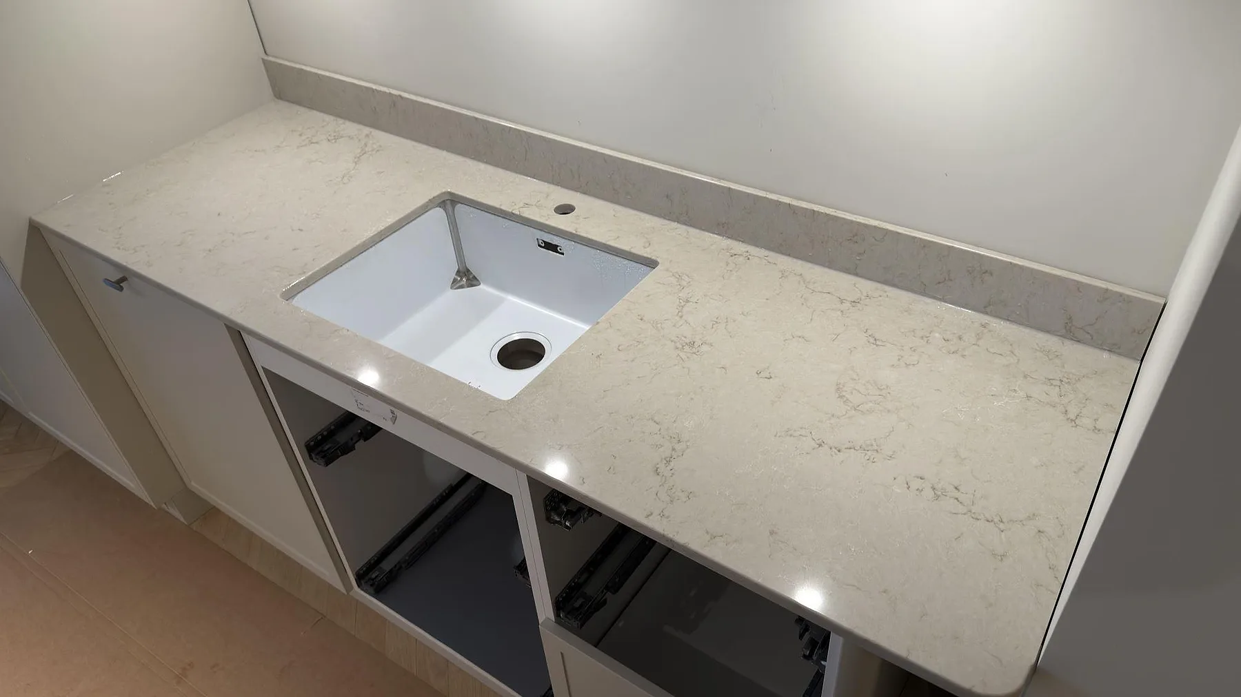 Närbild på polerad Caesarstone Taj Royale 5212 med ljus ådring, låg stänkkant och diskho i kök under montering i Stockholm.