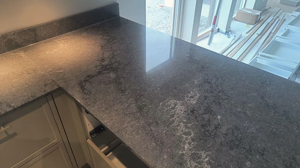 Peninsula och hörnyta i polerad Caesarstone Turbine Grey med ljus köksinredning under montering i Alingsås.