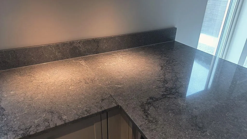 Närbild på polerad Caesarstone Turbine Grey som köksbänkskiva med mörk ådring och stänkkant i Alingsås.