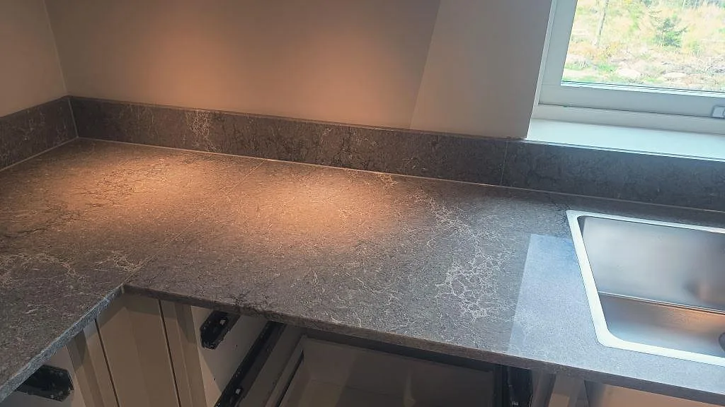Hörnbänkskiva i polerad Caesarstone Turbine Grey med rostfri diskho och stänkkant vid fönster i Alingsås.
