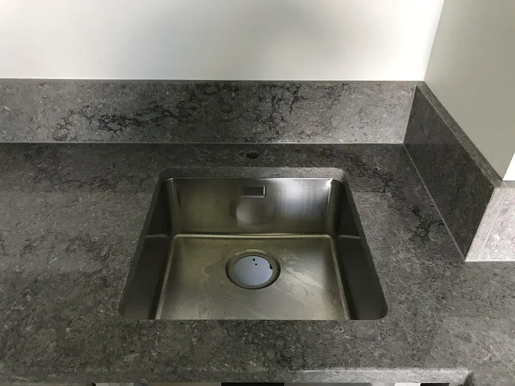 Detalj av kvadratisk underlimmad rostfri diskho i en köksbänkskiva av Caesarstone Turbine Grey, polerad mörkgrå kvartskomposit i Göteborg.