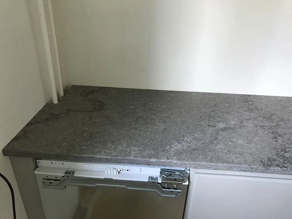 Köksbänkskiva i polerad Caesarstone Turbine Grey ovanför inbyggd diskmaskin i ett kök i Göteborg.