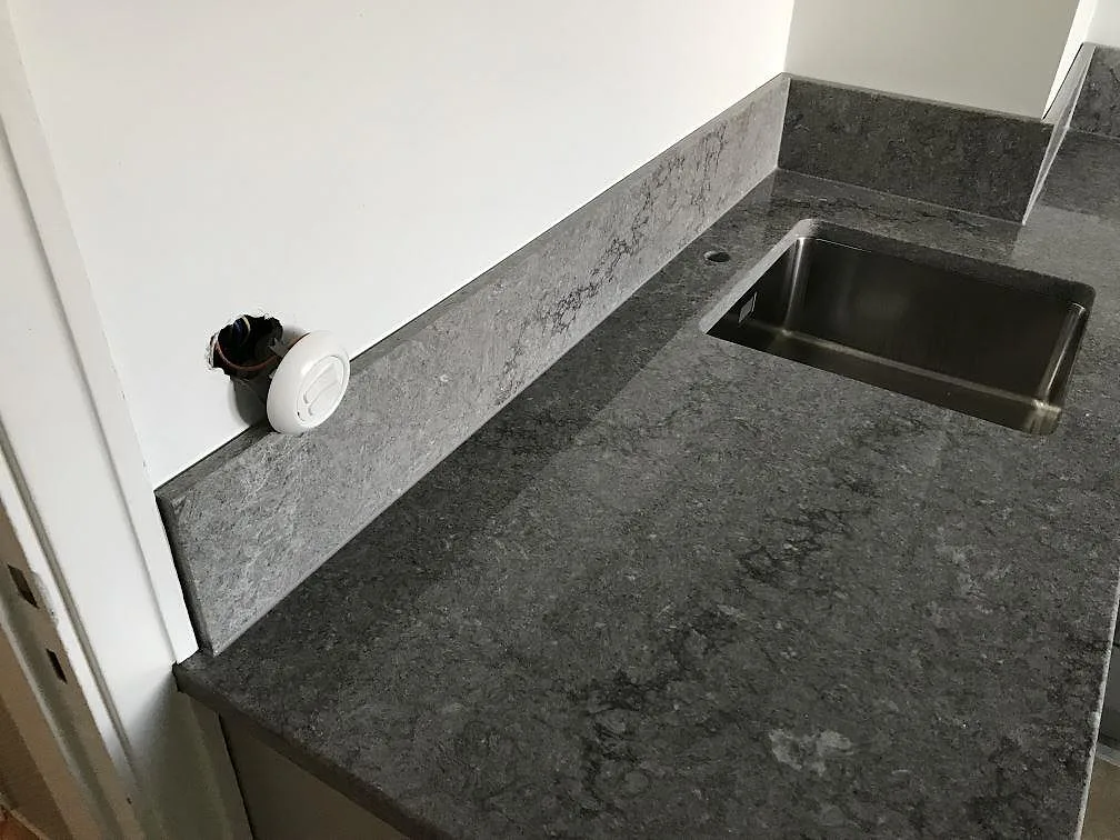 Köksbänkskiva i Caesarstone Turbine Grey, mörkgrå betongliknande kvartskomposit med polerad yta, med underlimmad rostfri diskho och uppvikt stänkkant i ett kök i Göteborg.