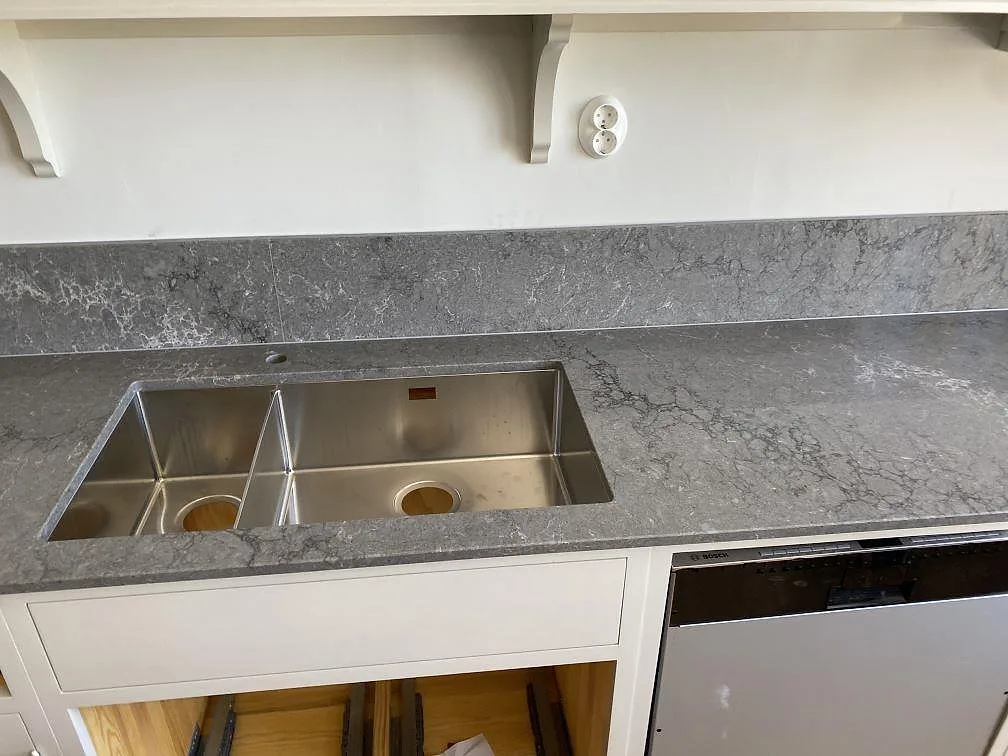 Underlimmad dubbel diskho i rostfritt stål i polerad köksbänkskiva av Caesarstone Turbine Grey med stänkskydd i samma sten i ett kök i Göteborg.