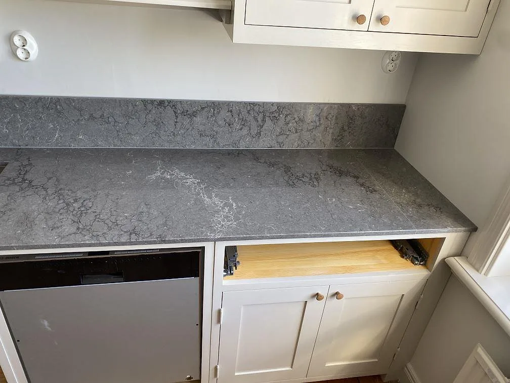 Köksbänkskiva i Caesarstone Turbine Grey med tydlig vit ådring och uppvikt stänkskydd över diskmaskinsplats i ett kök i Göteborg.