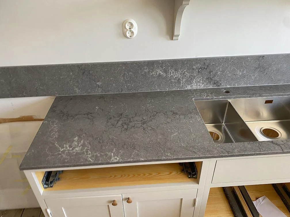 Polerad köksbänkskiva i grå kvartskomposit Caesarstone Turbine Grey med underlimmad rostfri diskho och uppvikt stänkkant i ett kök i Göteborg under montering.