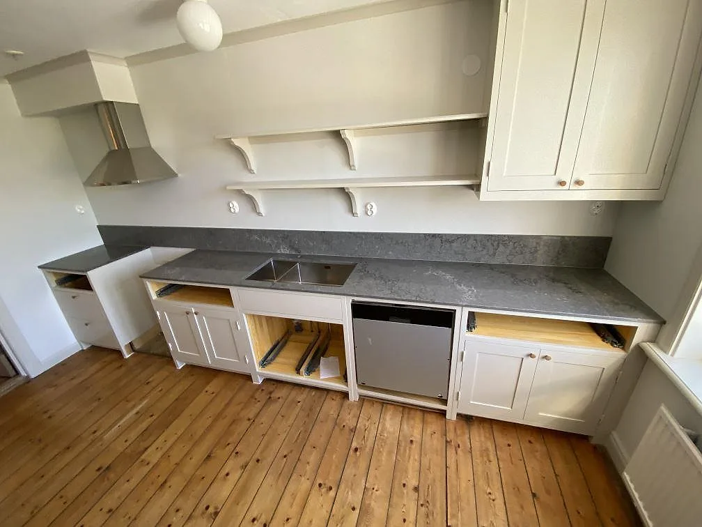 Köksbänkskiva i Caesarstone Turbine Grey, grå kvartskomposit med vita ådror, polerad, längs hela köksväggen med spiskåpa och uppvikt stänkskydd i ett kök i Göteborg under montering.